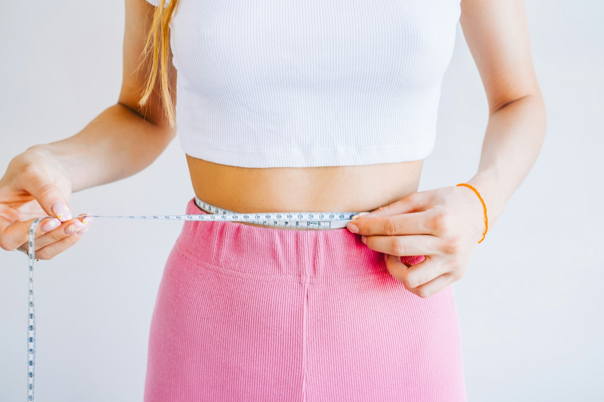 Slim woman measuring her waist's size with tape measure on white background. Successful weight loss